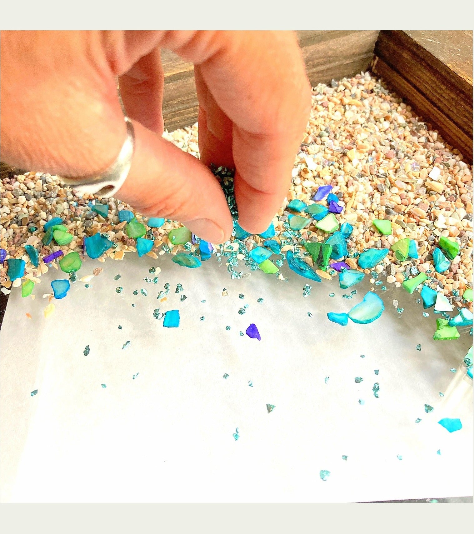 Hand arranging colorful glitter on a white surface with a wooden background